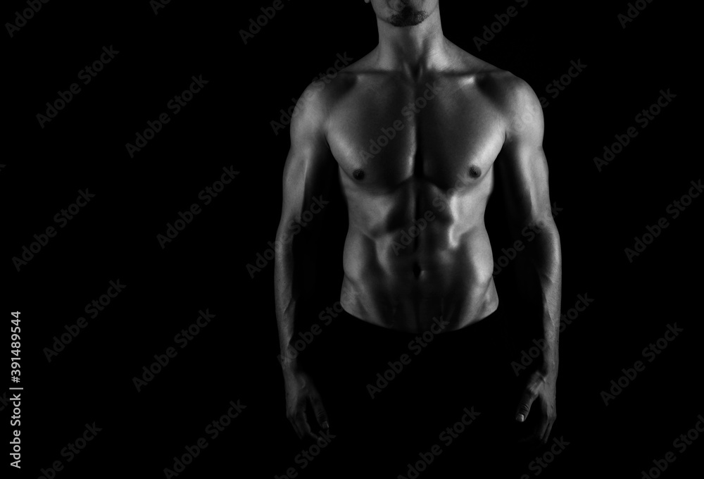 Muscular male torso of fit bodybuilder on black background in black and white