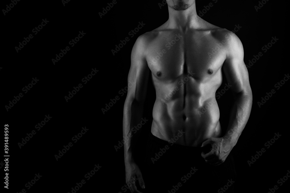Muscular male torso of fit bodybuilder on black background in black and white Muscular male torso of fit bodybuilder on black background in black and white