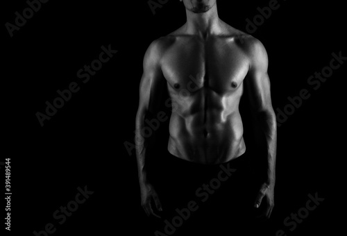 Muscular male torso of fit bodybuilder on black background in black and white