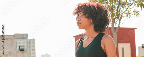 Quadro su tela Young African American woman looking far distance into the skyline buildings at rooftops