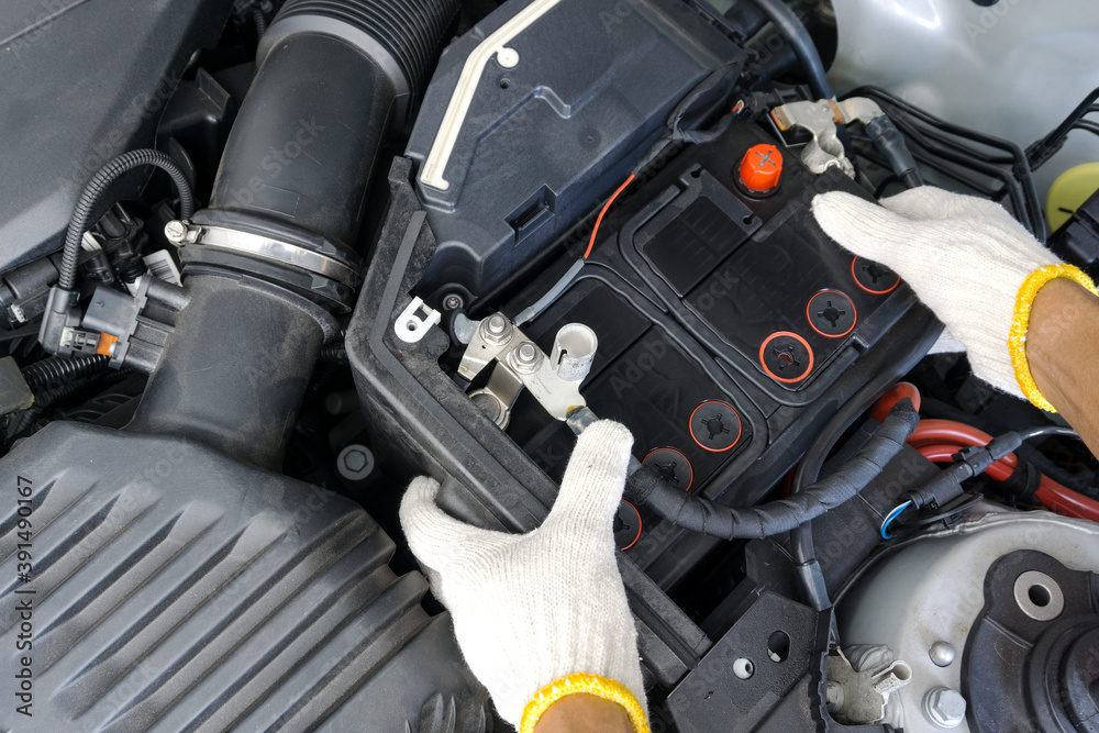 The auto mechanic is replacing the car battery in engine compartment. The auto mechanic is replacing the car battery in engine compartment.