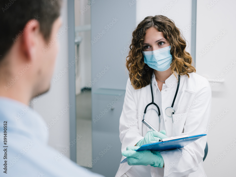 Junge Ärztin geht den Anamnesebogen mit einem neuen Patienten durch Junge Ärztin geht den Anamnesebogen mit einem neuen Patienten durch