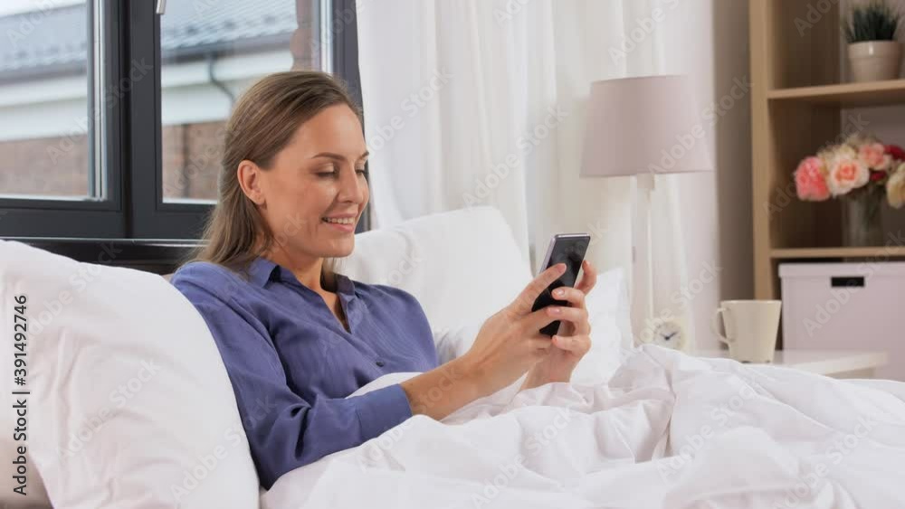 technology, internet, communication and people concept - happy young woman texting on smartphone in bed at home in morning technology, internet, communication and people concept - happy young woman texting on smartphone in bed at home in morning