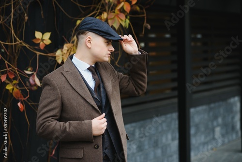 Foto A man posing in the image of an English retro gangster of the 1920s dressed in Peaky blinders style near old brick wall