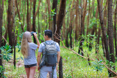 Young couple hiking trough forest and watching birds with binoculars. © sutthichai