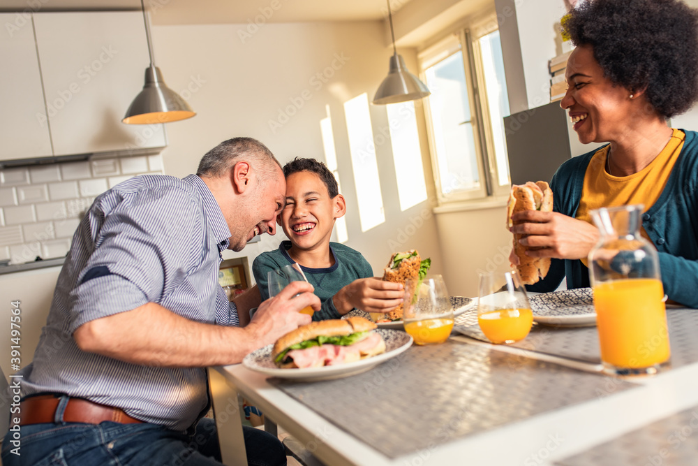 Smiling mixed race family sitting at the kitchen table having breakfast at home.	