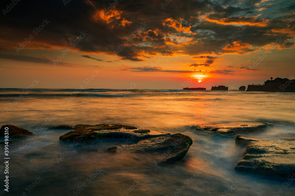 Calm ocean long exposure. Stones in mysterious mist of the sea waves. Concept of nature background. Sunset scenery background. Sun on horizon. Mengening beach, Bali, Indonesia.