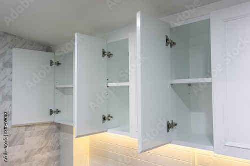 New white shelves, open the door which is empty inside, in the modern kitchen, orange lights below.