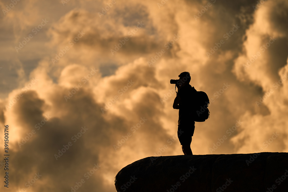 silhouette of photographer taking picture of landscape on the peak of mountain during sunset