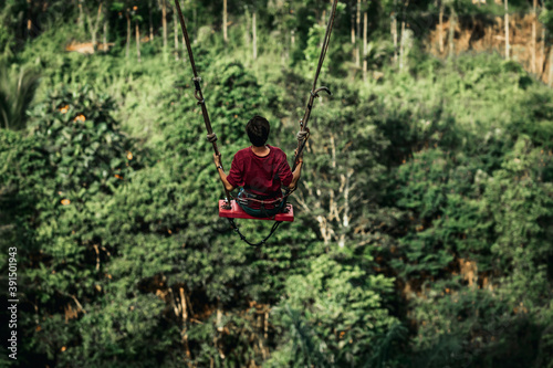 Young man swinging in the jungle rainforest of Bali island, Indonesia. Swing in the tropics. Swings - trend of Bali island.
