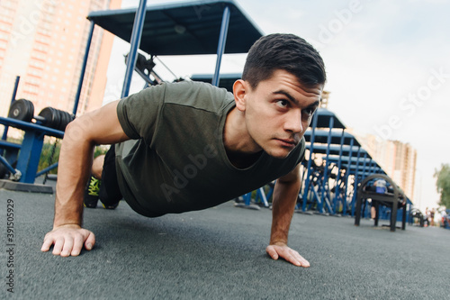 A young man does push-ups on the street on a specialized sports ground with trainers. Build muscles in the fresh air. Sport and healthy lifestyle concept