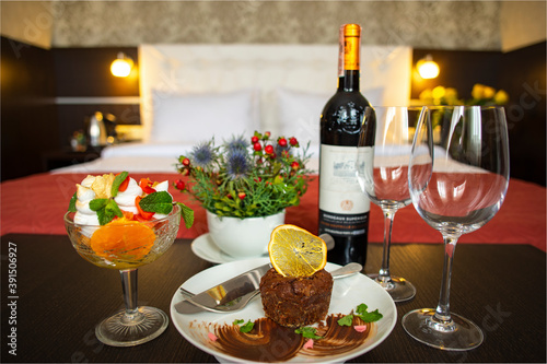 Wine with groceries and a sweet dessert in the hotel room on the background of a double bed. Luxury bedroom with red wine as background.