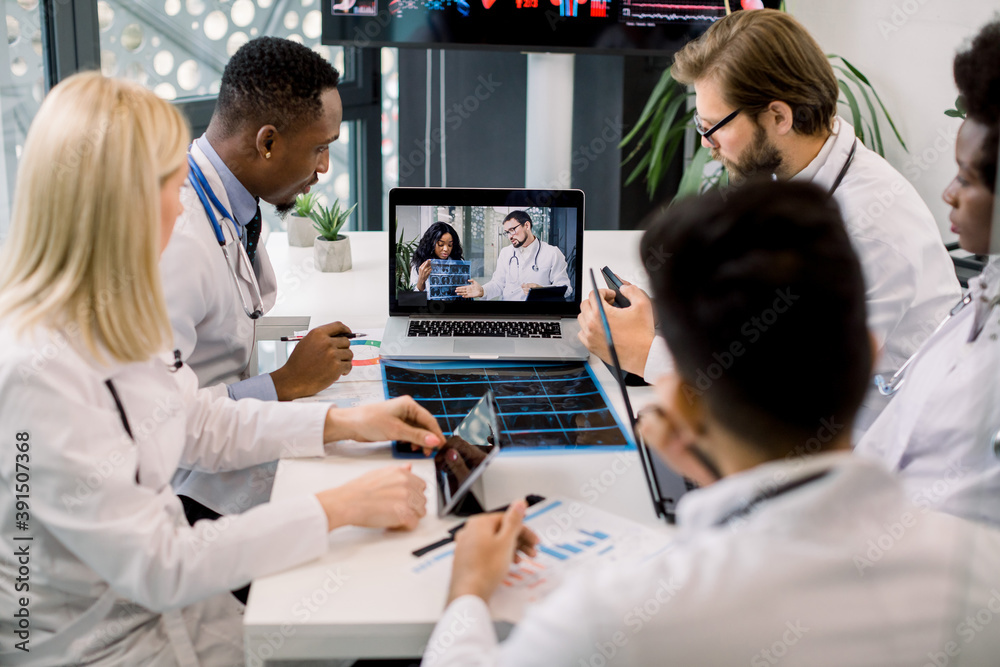 Top angle view of five multiracial confident doctors discussing CT scan results of patient while having video conference meeting with their Afrcian and Caucasian colleagues. Telemedicine, video chat