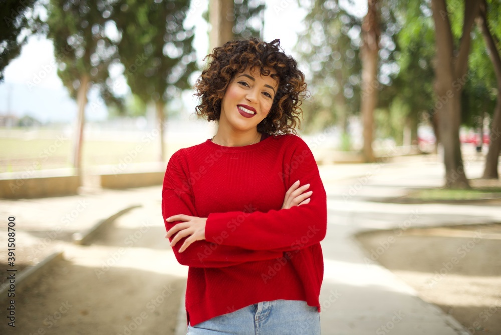 Young arab woman wearing casual red sweater in the street, happy face smiling with crossed arms looking at the camera. Positive person. Young arab woman wearing casual red sweater in the street, happy face smiling with crossed arms looking at the camera. Positive person.