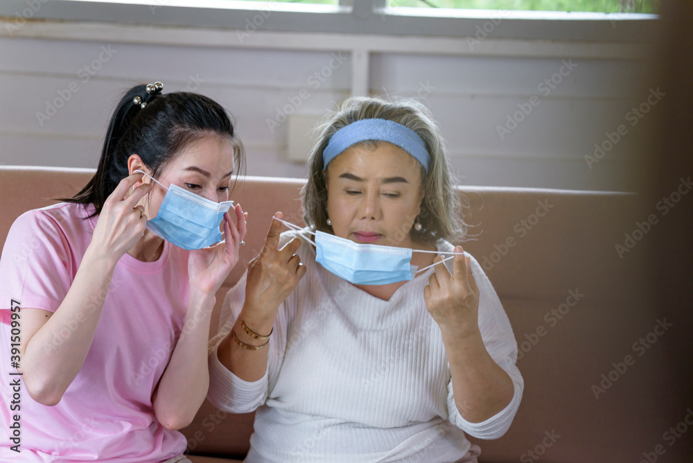 Asian young woman teach older mother, how to wear face mask from online learn in living room with carefully. family concept