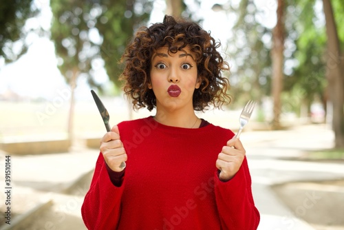 Young beautiful Arab woman standing outdoors wearing red sweater hungry girl holding in hand fork knife want tasty yummy pizza pie © Roquillo