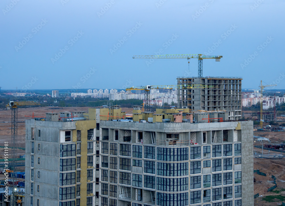 View on the large construction site at urban area in the evening. Tower cranes in action with machinery and builders. Multi-storey residential Building is being constructed use of crane.
