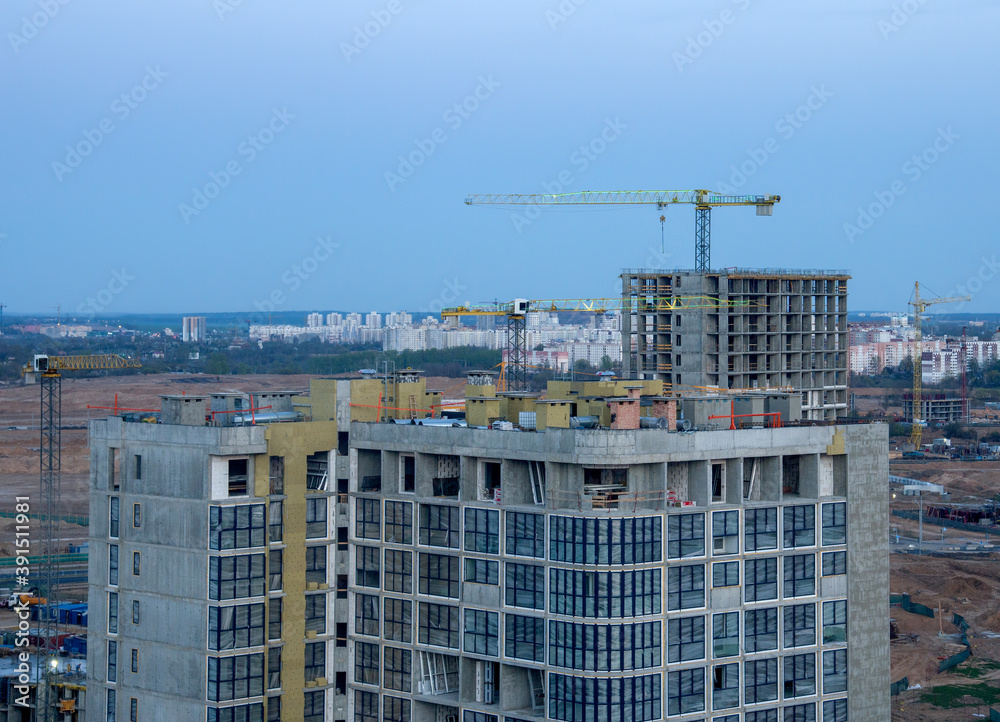 View on the large construction site at urban area in the evening. Tower cranes in action with machinery and builders. Multi-storey residential Building is being constructed use of crane. View on the large construction site at urban area in the evening. Tower cranes in action with machinery and builders. Multi-storey residential Building is being constructed use of crane.