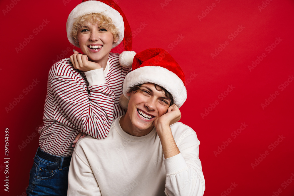 Beautiful happy couple in Santa Claus hats smiling at camera Beautiful happy couple in Santa Claus hats smiling at camera