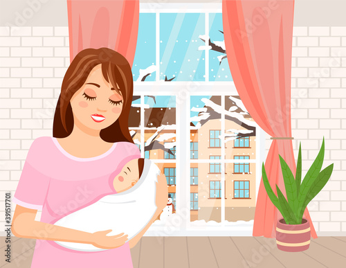 Mom holding in her arms a small baby is standing in the room. Newborn in a tender embrace of mother. Happy young woman with an infant is standing indoors against a window with a winter landscape