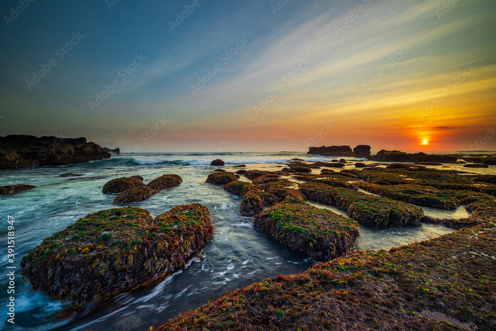 Amazing seascape. Ocean with moving wave. Low tide. Stones covered by green moss and seaweeds. Sun on horizon. Sunset scenery background. Long exposure. Mengening beach, Bali Amazing seascape. Ocean with moving wave. Low tide. Stones covered by green moss and seaweeds. Sun on horizon. Sunset scenery background. Long exposure. Mengening beach, Bali