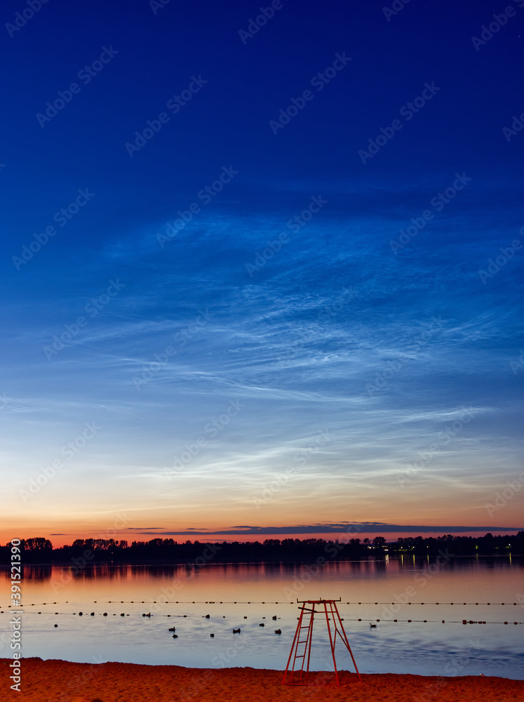 Noctilucent clouds also known as a night shining clouds over a lake.
