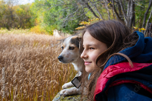 a small dog and a girl together in an embrace look in the same direction in the autumn Park. Close up.