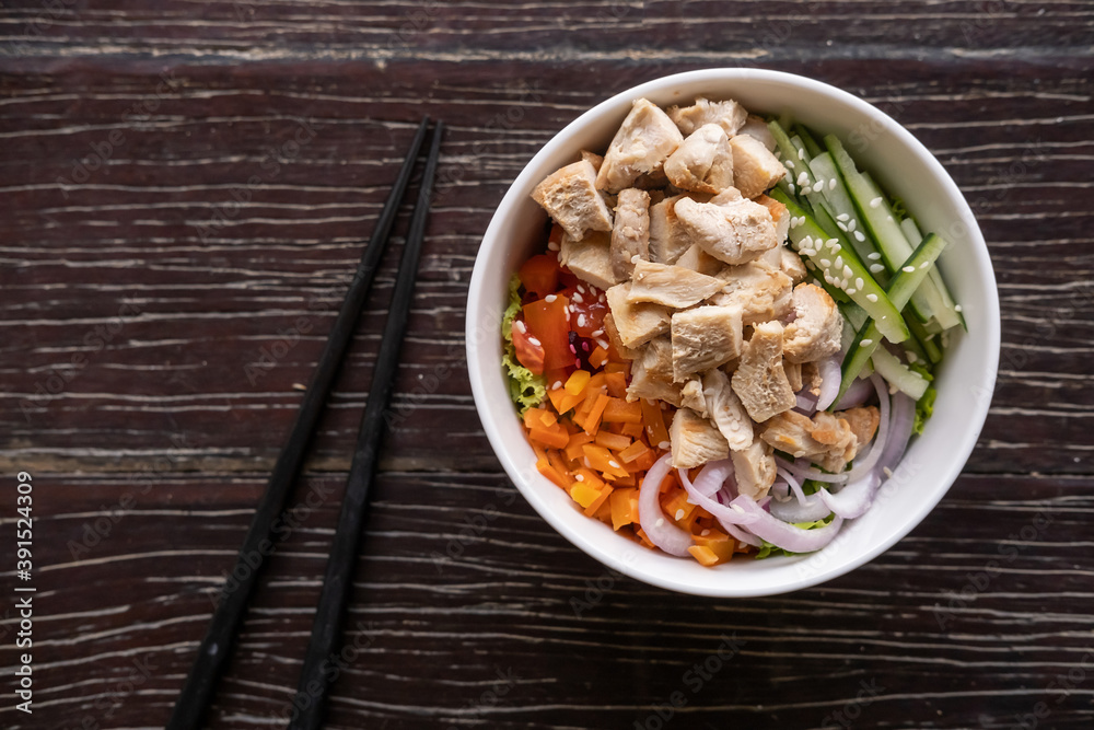 Healthy organic chicken poke bowl with cucumber, rice, carrots, onion served in bowl on wooden table. Healthy lifestyle