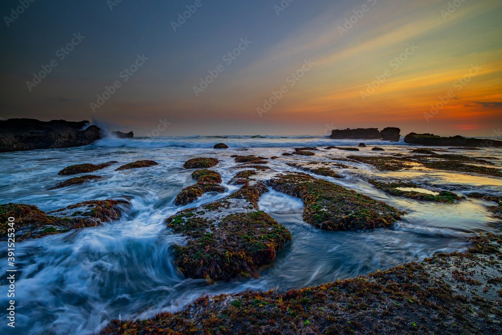 Amazing seascape. Ocean with moving wave. Low tide. Stones covered by green moss and seaweeds. Concept of nature background. Sunset scenery. Long exposure. Mengening beach, Bali