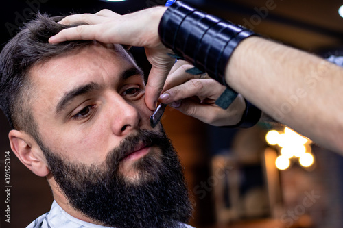 Fotografia Young bearded man getting haircut by professional at modern barbershop