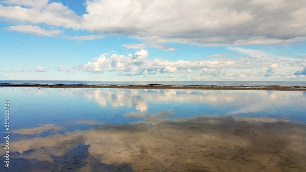 Calm sea on a sunny summer day. Blue cloudy sky reflection in tranquil water. Holiday and travel concept. Latvian nature.