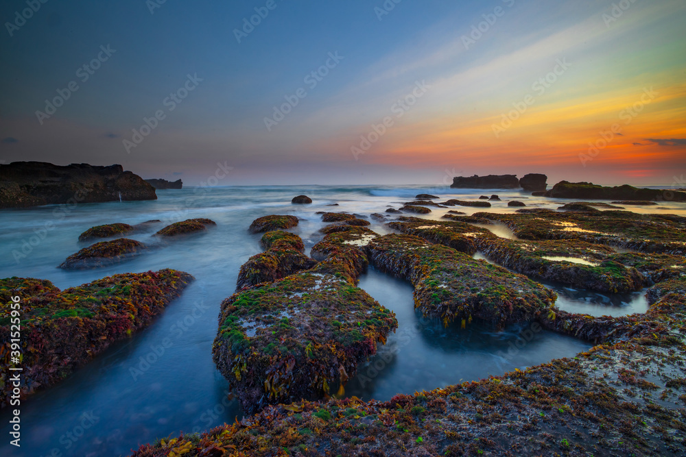 Beautiful seascape. Ocean with motion waves. Low tide. Stones covered by green moss and seaweeds. Concept of nature background. Sunset view. Long exposure. Mengening beach, Bali