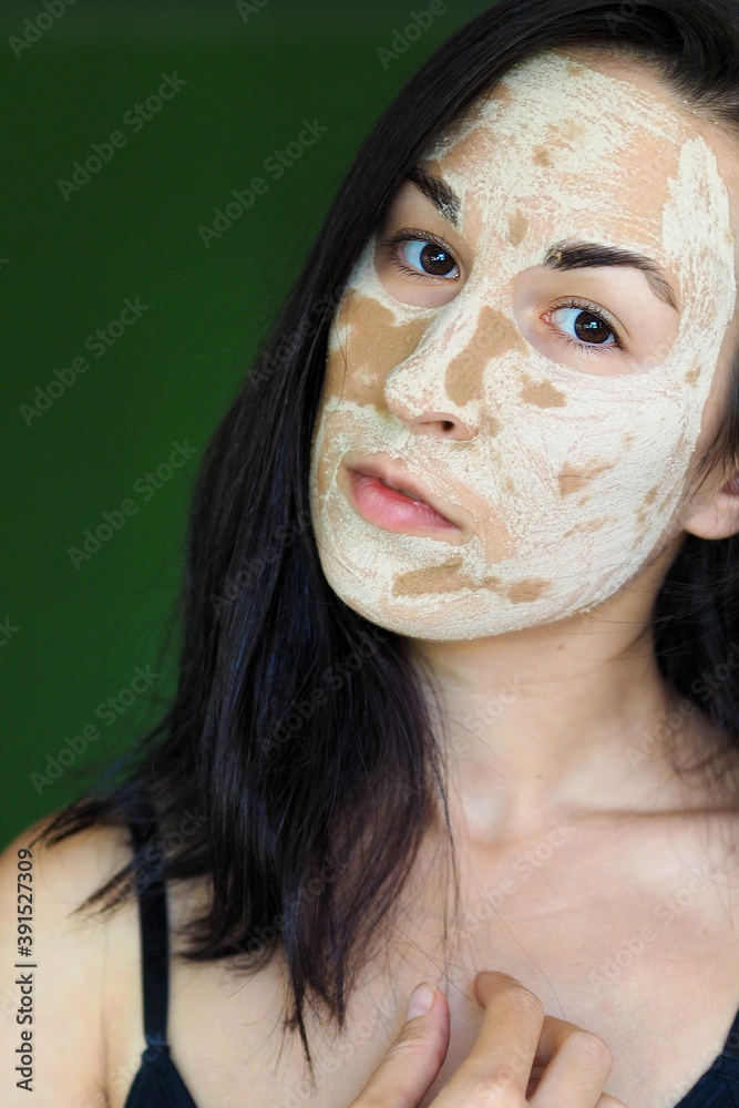 Fototapeta premium young brunette woman with a clay homemade mask on her face looks into the frame