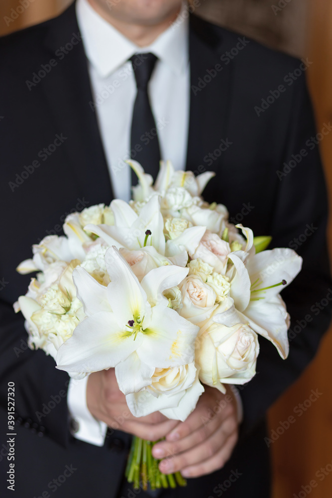 The groom holding a wedding bouquet of flowers in his hands, waiting for his bride. bridal bouquet of white lilies and daisies The groom holding a wedding bouquet of flowers in his hands, waiting for his bride. bridal bouquet of white lilies and daisies