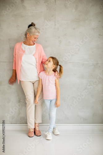 Little girl with her grandmother standing by the wall