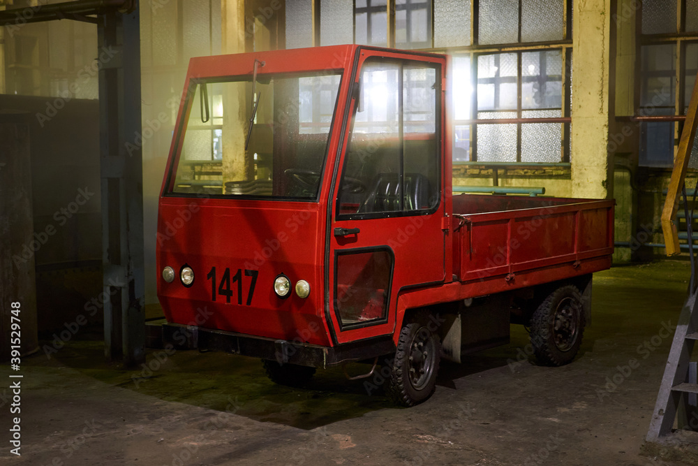 GRODNO, BELARUS - NOVEMBER 2020: Vintage old fashioned style red cargo electric car truck stands into warehouse late at night at factory or plant.