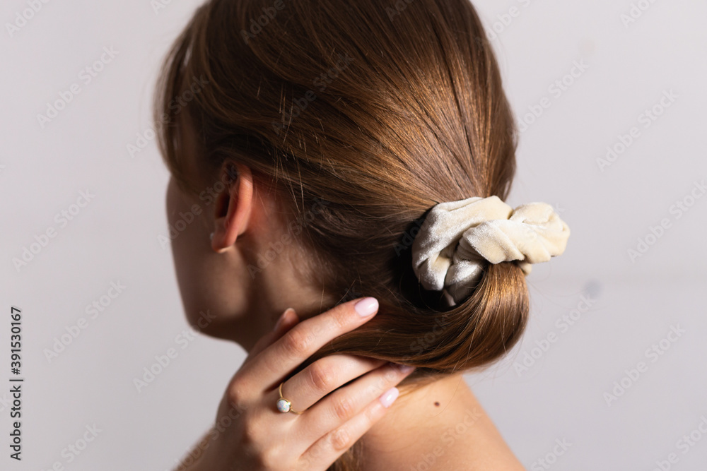 Naklejka premium Natural blond woman holding her amazing hair in ponytail with beige scrunchie. Side perspective. White background.