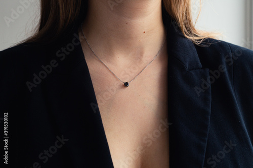 Silver necklace with black stone pendant on woman’s neck, black blazer, elegant style. close-up. Business power woman, successful people