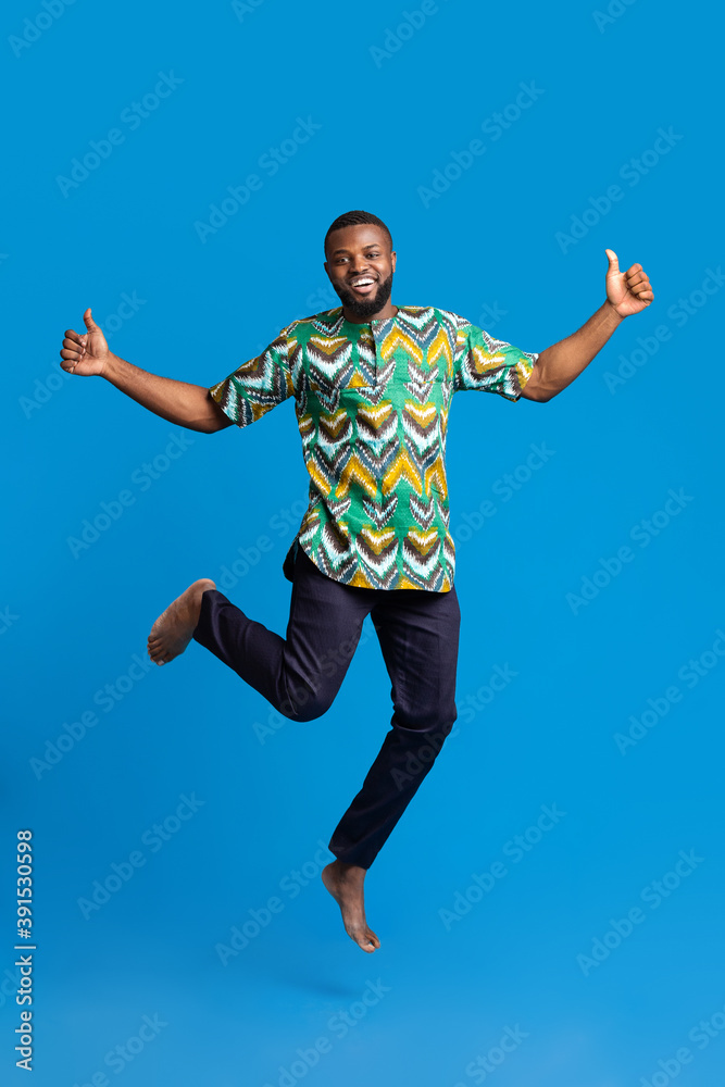 Fototapeta premium Positive black man jumping up over blue