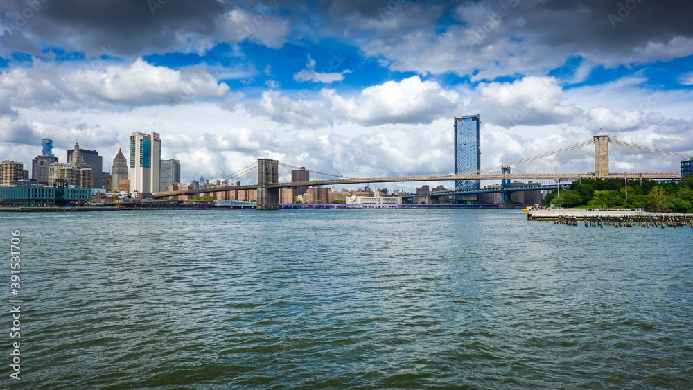 View from Brooklyn Bridge to Manhattan in New York during sunny day with blue sky and white clouds