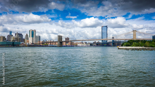 View from Brooklyn Bridge to Manhattan in New York during sunny day with blue sky and white clouds photo