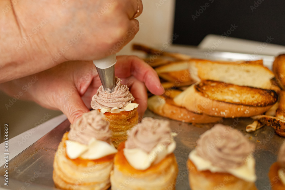 Baskets of puff pastry with butter and pate. Baking on a tray, black. A woman decorates baking with a rose of pate.