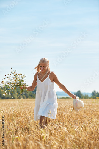 Fototapeta Naklejka Na Ścianę i Meble -  Beautiful woman in hat and with a basket of field daisies in sunny summer day.