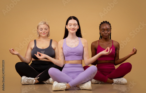 Beautiful body positive women of different size and appearances meditating together indoors