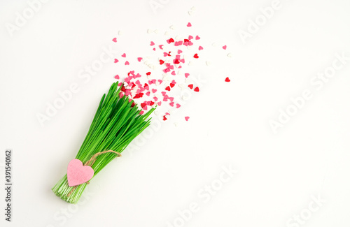 Small hearts above a bouquet of green grass on a light background. The view from the top. Concept of holiday backgrounds.