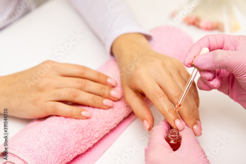 Close-up of a manicurist applying moisturizing nail oil on person's hand. On the photo we see pink towel