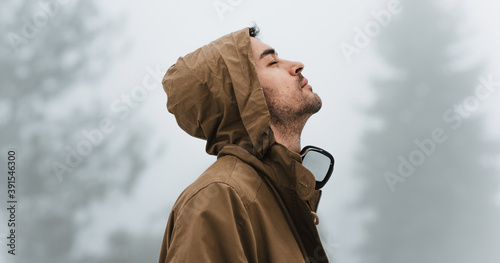 Vászonkép Side view of a handsome male walking in misty nature, listening to the music on his headphones with closed eyes outside