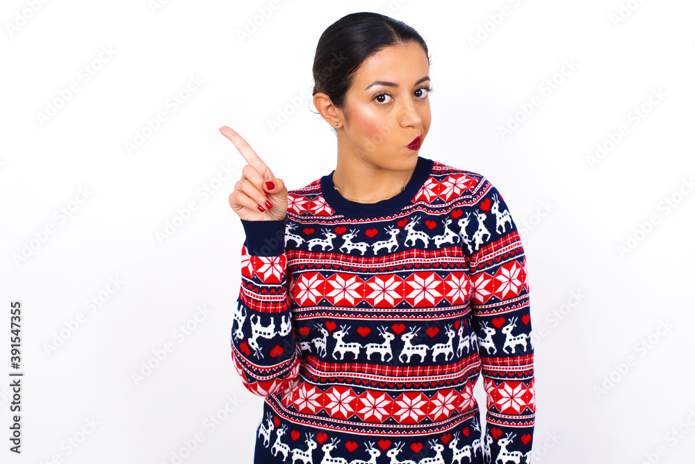 No sign gesture. Closeup portrait unhappy Young beautiful Arab woman wearing Christmas sweater against white wall raising fore finger up saying no. Negative emotions facial expressions, feelings. No sign gesture. Closeup portrait unhappy Young beautiful Arab woman wearing Christmas sweater against white wall raising fore finger up saying no. Negative emotions facial expressions, feelings.