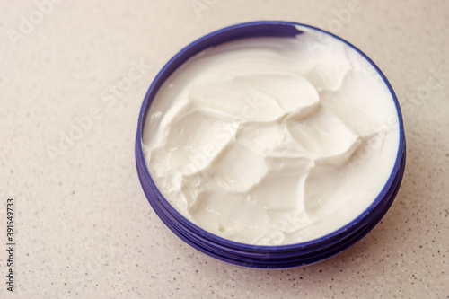 Open round container with white cream on a marble table.