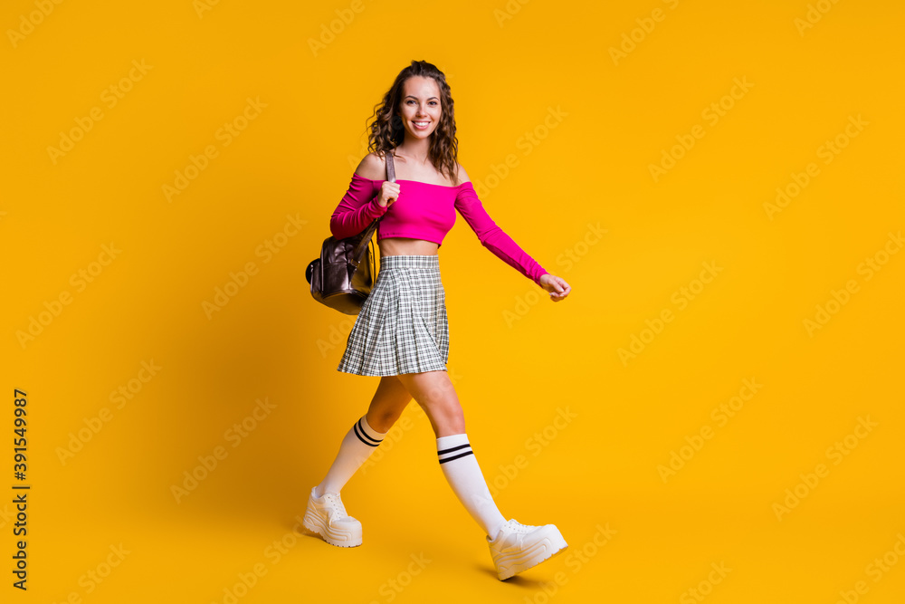 Full length photo of pretty sweet lady hold rucksack walk beaming smile wear pink top uncovered shoulders mini skirt stockings sneakers isolated yellow color background